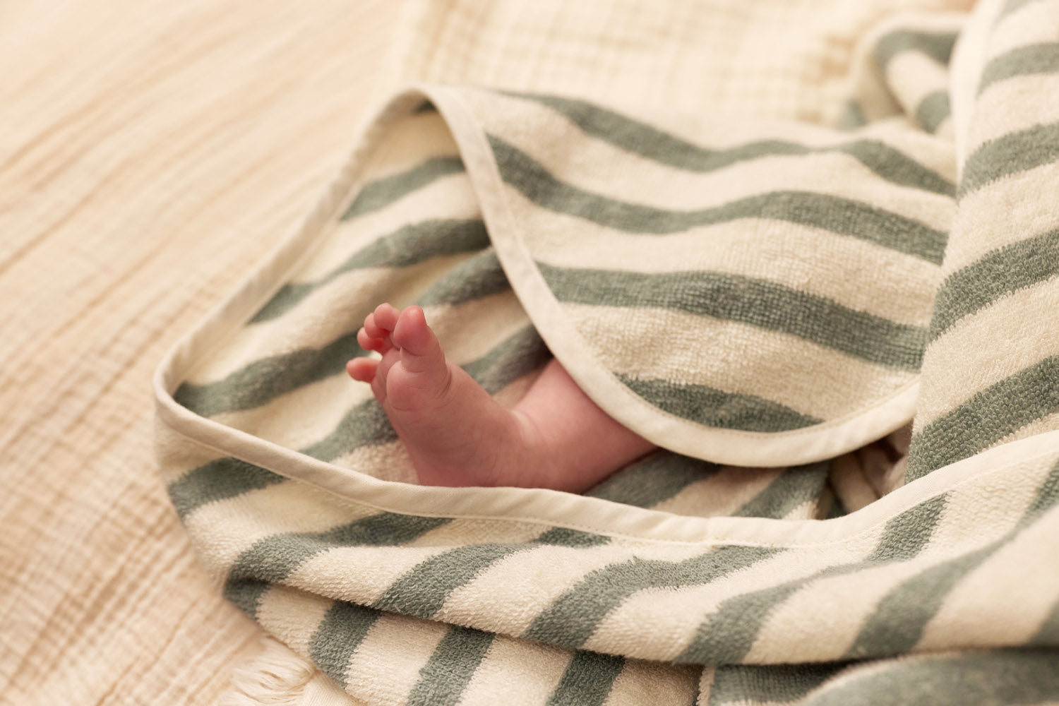 Sfeerbeeld van voetjes na badmoment in organisch katoen badcape, sea green met strepen