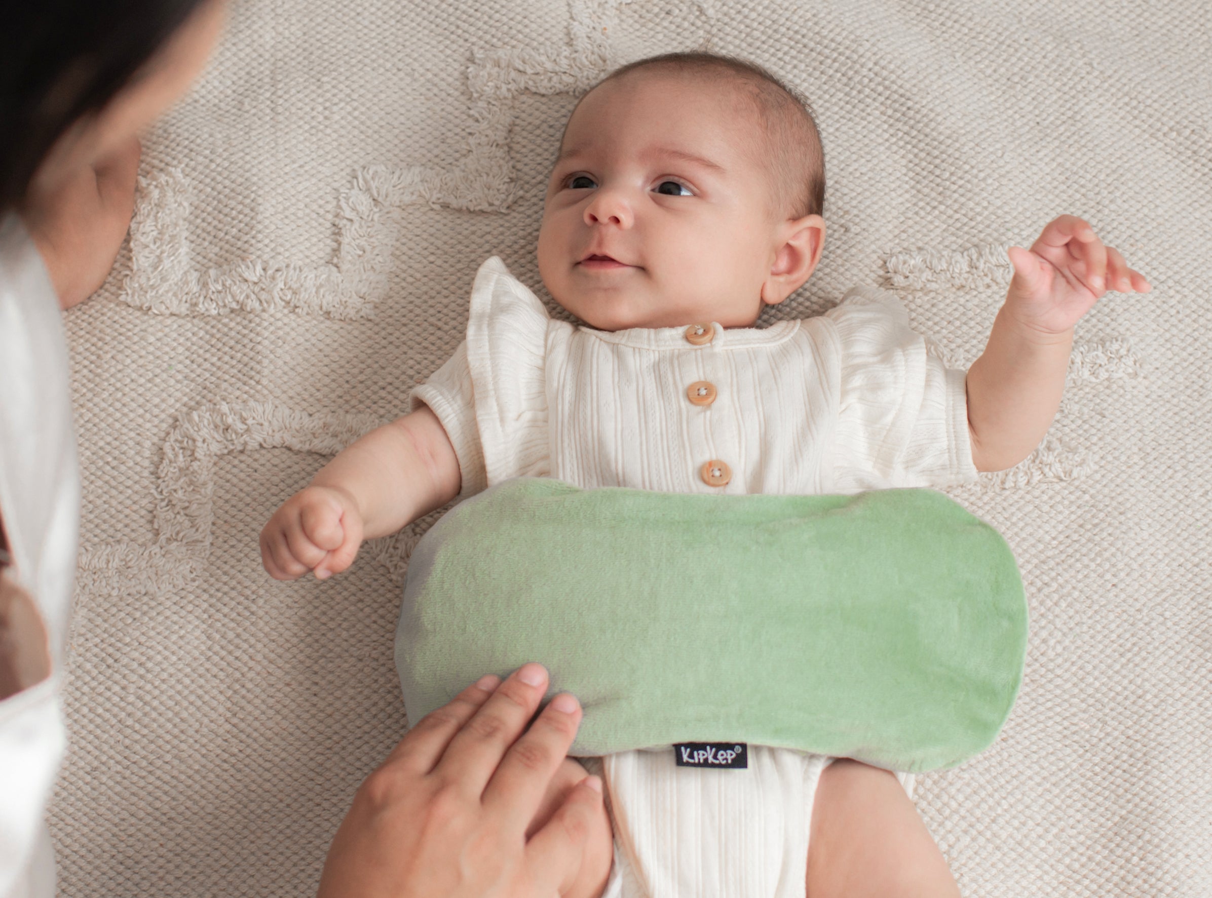 Sfeervol beeld van baby met zachtgroen KipKep warmtekussen, hoes van biologisch katoen zichtbaar