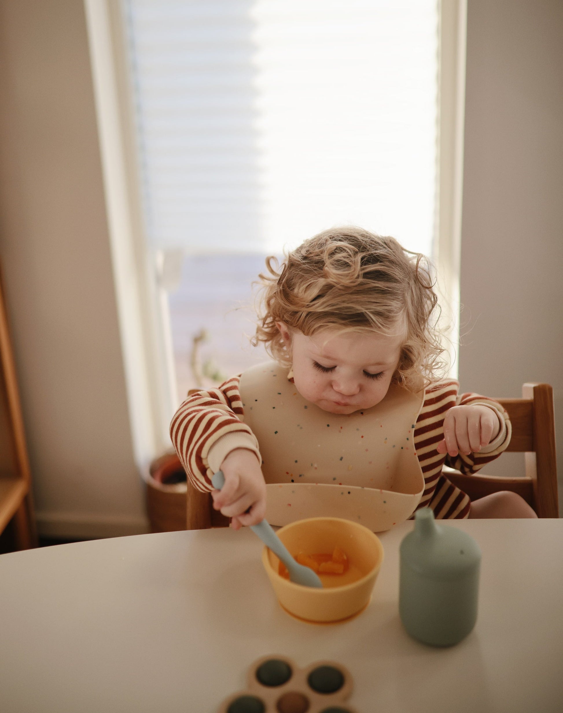 kindje heeft siliconen confetti slabber om van mushie tijdens het eten